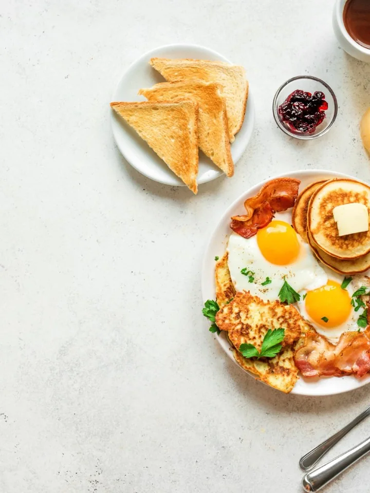 Fried eggs with bacon, pancakes, a hash brown and toast on a white plate